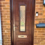 Brown composiate front door with vertical panels and a rectangular glass panel featuring a diamond pattern. The door has a silver handle, letterbox, and a small silver plate