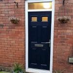 Blue composite front door with four raised panels and a glazed top light. The door has a silver handle, letterbox, and is framed by white trim.