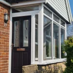 Black composite front door with glass panels in a white porch extension.