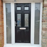 A black composite front door with a glazed panel and letterbox, surrounder by a white pvc frame with frosted glass, flanked by brick walls and a sidelight window