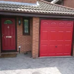 Front view of a garage door and composite door in red, a grey block driveway, a small tiled roof overhang