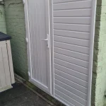 White paneled pvc door and adjacent wall paneling in an outdoor area, next to a light green brick wall."