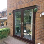 French doors with dark frames on a brick exterior wall, leading to an outdoor patio, decorated with hanging topiary balls on either side.
