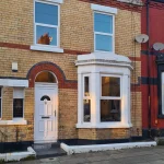 A two-story terrist brick house with white pvc windows. The house has large bay style window on the ground floor