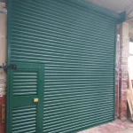 Green Roller Shutter Door factory entrance, with a small door within the main roller shutter, brick on the side and concrete entrance