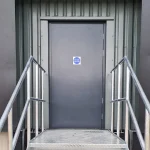Dark Grey Fire Escape door or steel door, a front on view with the top of a steel stair case and two steel bannisters, one either side showing